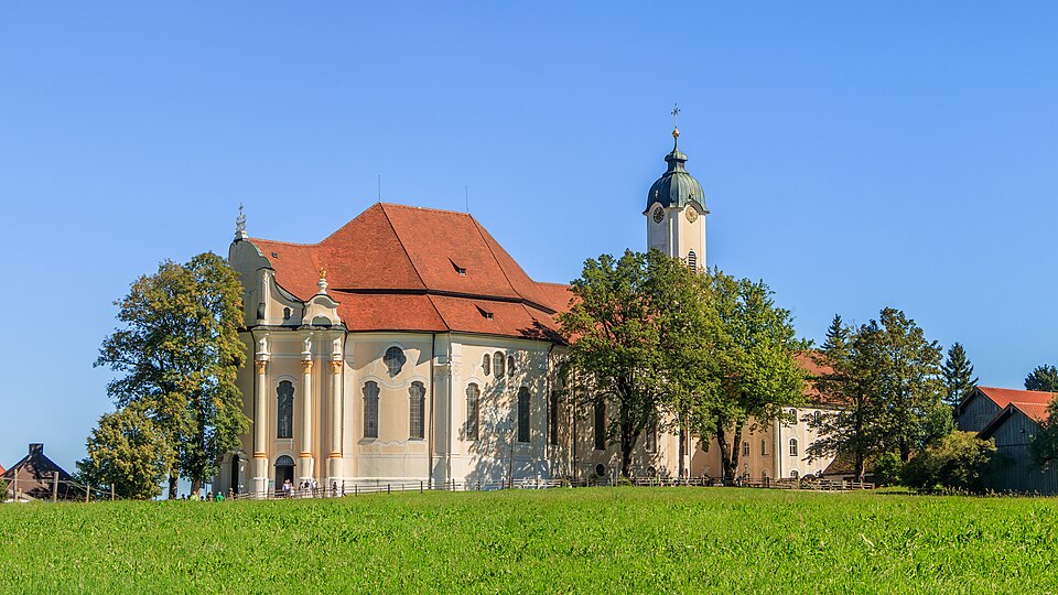 The white rococo Wieskirche standing alone in a green Alpine meadow.